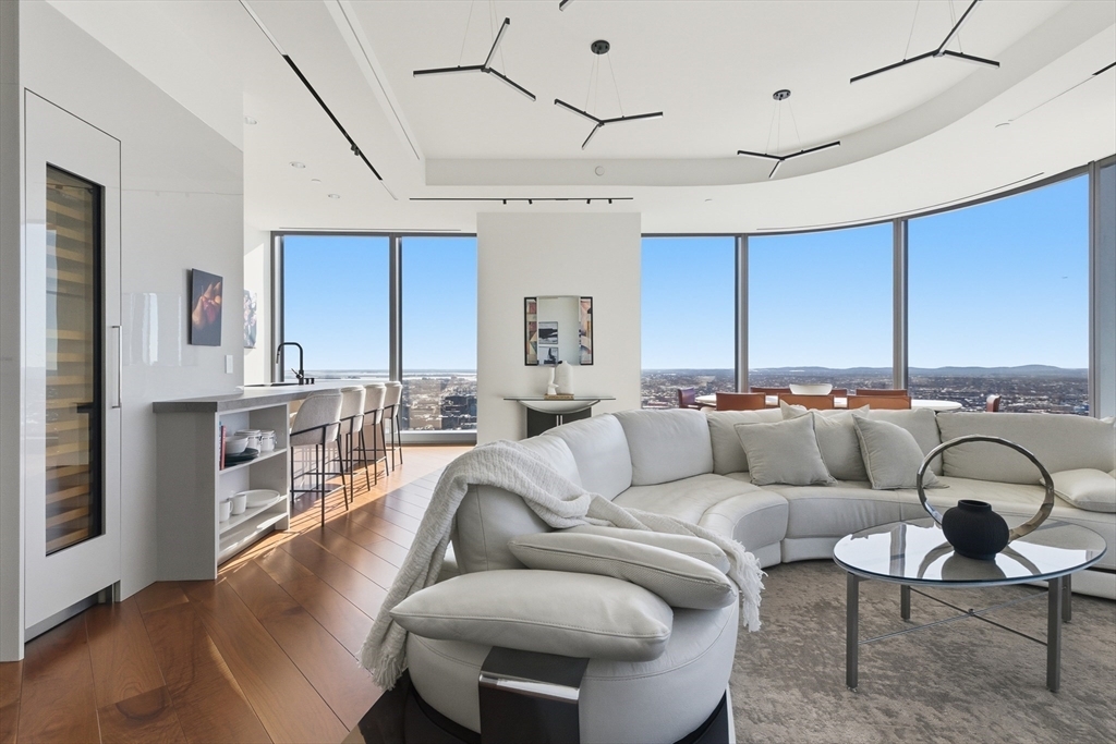 Welcome to the 42nd floor of the Four Seasons Private Residences at One Dalton. This south-facing corner residence offers 2 spacious bedrooms, a den, and breathtaking panoramic city views filled with natural light throughout the day. Expansive exposures allow residents to experience both sunrise and sunset from the home, casting beautiful light across the skyline from morning through evening. The open floor plan is framed by dramatic 11-foot floor-to-ceiling windows, wide-plank walnut hardwood floors, and a striking double-sided gas fireplace with a marble surround. The kitchen is appointed with upgraded Dekton countertops and Wolf and Sub-Zero appliances. Residents enjoy world-class amenities including 24/7 concierge and doorman service, on-site valet parking, in-residence dining, a 50th-floor private lounge, and dedicated in-building storage, in addition to a full-service spa, indoor pool, fitness center, and golf simulator.