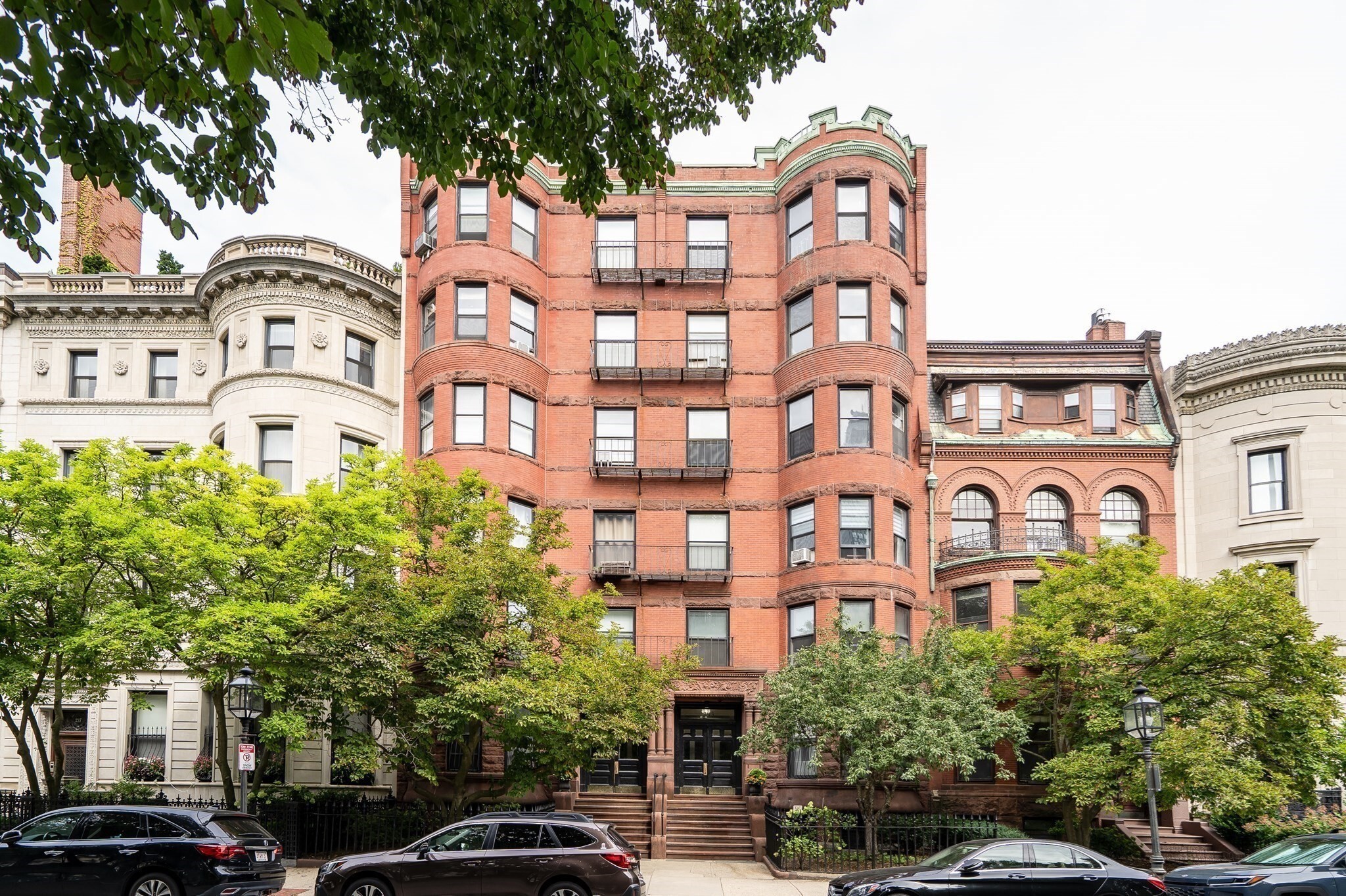 Front-facing studio on the sunny side of iconic Commonwealth Avenue, featuring high ceilings and very large bay windows overlooking the Commonwealth Avenue Mall and trees. A recessed area provides space to partially tuck away a bed while preserving more of the main living area. A brick accent wall and original oversized fireplace mantel with ornate wood detailing add architectural character. The kitchen includes a four-burner gas stove, refrigerator/freezer, room for a table and a ceiling fan with light. Two closets provide excellent storage, including one that could serve as a pantry and another deep closet. Full tiled bathroom with tub. Easy access from the building lobby without any stairs. Ideally situated in a prime Back Bay location just off Gloucester Street.