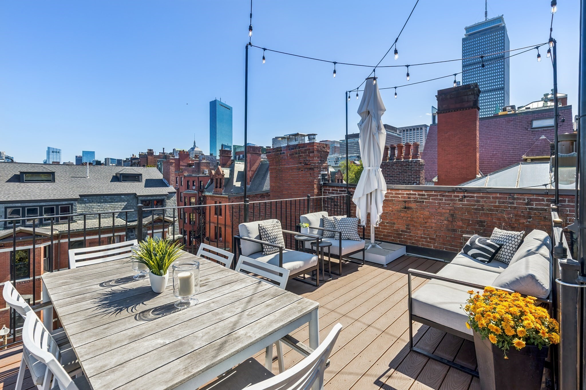 This penthouse duplex, offering 2 beds plus a generous den and a private roof deck, sits discreetly tucked on one of Back Bay's beloved side streets in a low-stoop brick rowhome—a rare opportunity to enjoy penthouse living without the penthouse climb. Upon entering, you are welcomed into a spacious foyer with room for all the coats and boots New England's seasons require. Around the corner, a beautifully appointed kitchen offers island seating, plenty of counter space and abundant cabinet storage. The kitchen flows seamlessly into the dining area and unfolds into the fireplaced living room, where skyline views and custom built-ins add both beauty and storage. Before heading up the custom staircase, strikingly set against exposed brick, you'll find a half bath and a sizable den that shares the same city views.The upper level features the primary bedroom with a vaulted wood-plank ceiling, an outfitted walk-in closet and a dual-entry full bath, accessible from both the bedroom and the hall. The second bedroom, with custom closets and eaves storage, sits next to the renovated second full bath. Thoughtful luxuries abound: double ovens, heated bathroom floors, a heated towel rack, and wine and beverage coolers tucked into the hall storage, perfectly placed for entertaining on the private roof deck. Large enough for both lounge and dining areas, the deck is ideally situated for Fourth of July fireworks and offers a year-round treetop perspective. Rounding out the home are in-unit laundry, common laundry and storage in the basement, a transferrable rental parking space nearby and a recently installed high-efficiency HVAC system, in a 100% owner-occupied building.  All of this sits a block from the Commonwealth Avenue Mall and less than two blocks from Newbury Street's boutiques, restaurants and cafes, with The Prudential Center, the Esplanade and Fenway Park all nearby. Commuters enjoy quick access to the Mass Pike and Storrow Drive. This is Back Bay living at its best.